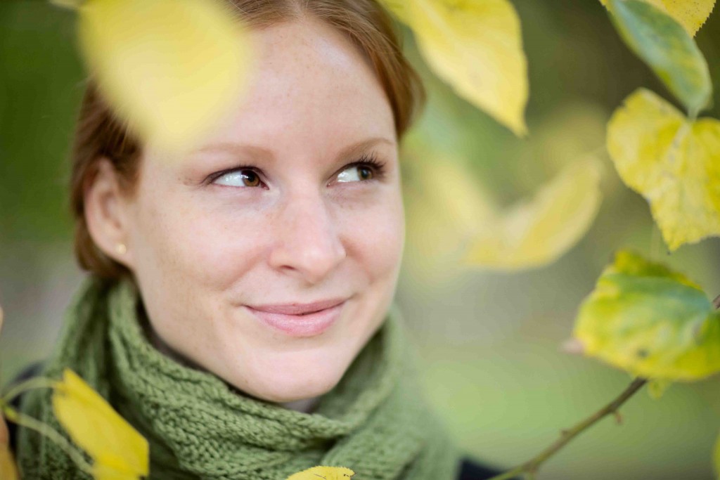 Closeup portrait among colored leaves of a happy young woman with red hair wearing a green scarf.